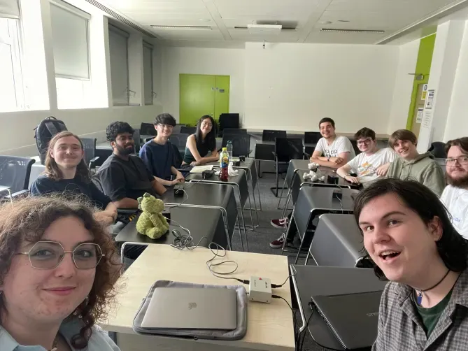 A group of student quizzers sat in a seminar room at Royal School of Mines, London. The student groups are Imperial A and Edinburgh B. Two moderators appear in the image.