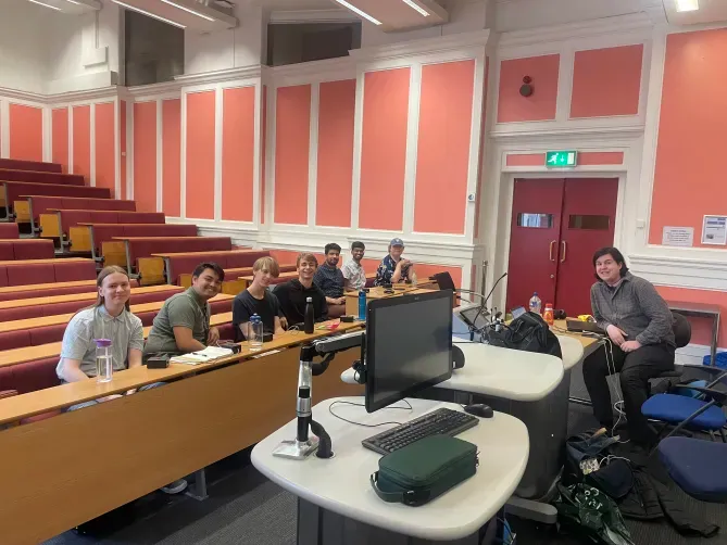 A group of student quizzers sat in a lecture theatre at Royal School of Mines, London. The student groups are Warwick A and Manchester A. One moderator appears in the image.